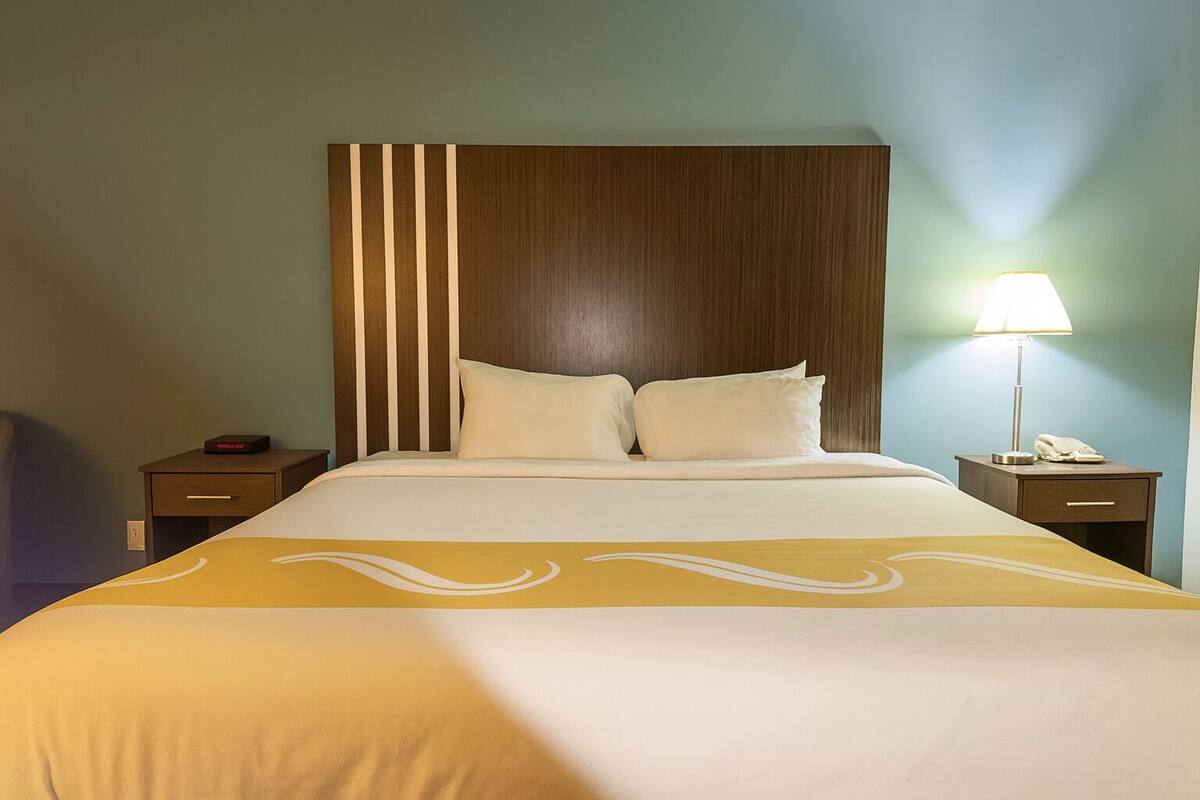 A hotel room with a large bed, two bedside tables, a nightstand, and a lamp.