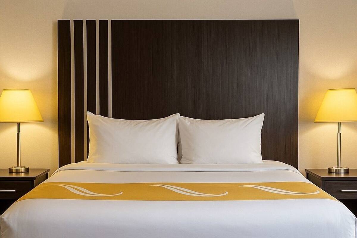 A hotel room with a large bed, two bedside lamps, and a dark headboard.