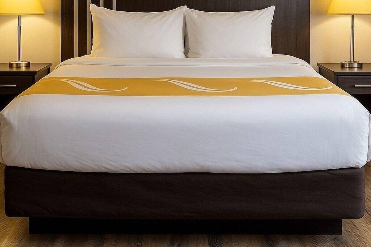 A hotel room with a large bed, two bedside lamps, and a dark headboard.