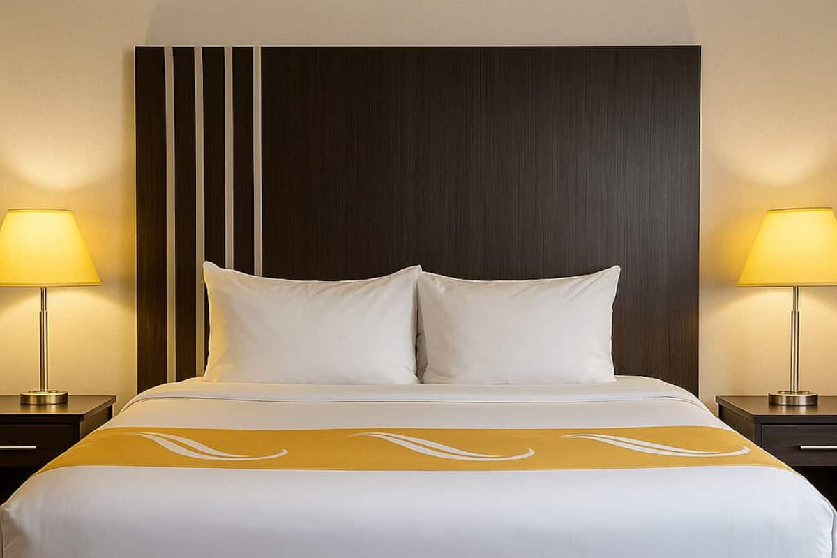 A hotel room with a large bed, two bedside lamps, a dark headboard, and a wooden floor.