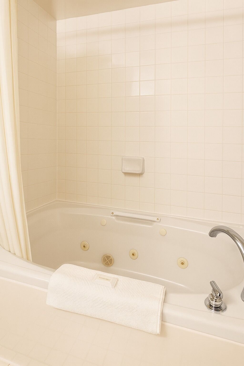 A bathroom with a bathtub, a handrail, a faucet, and a towel.