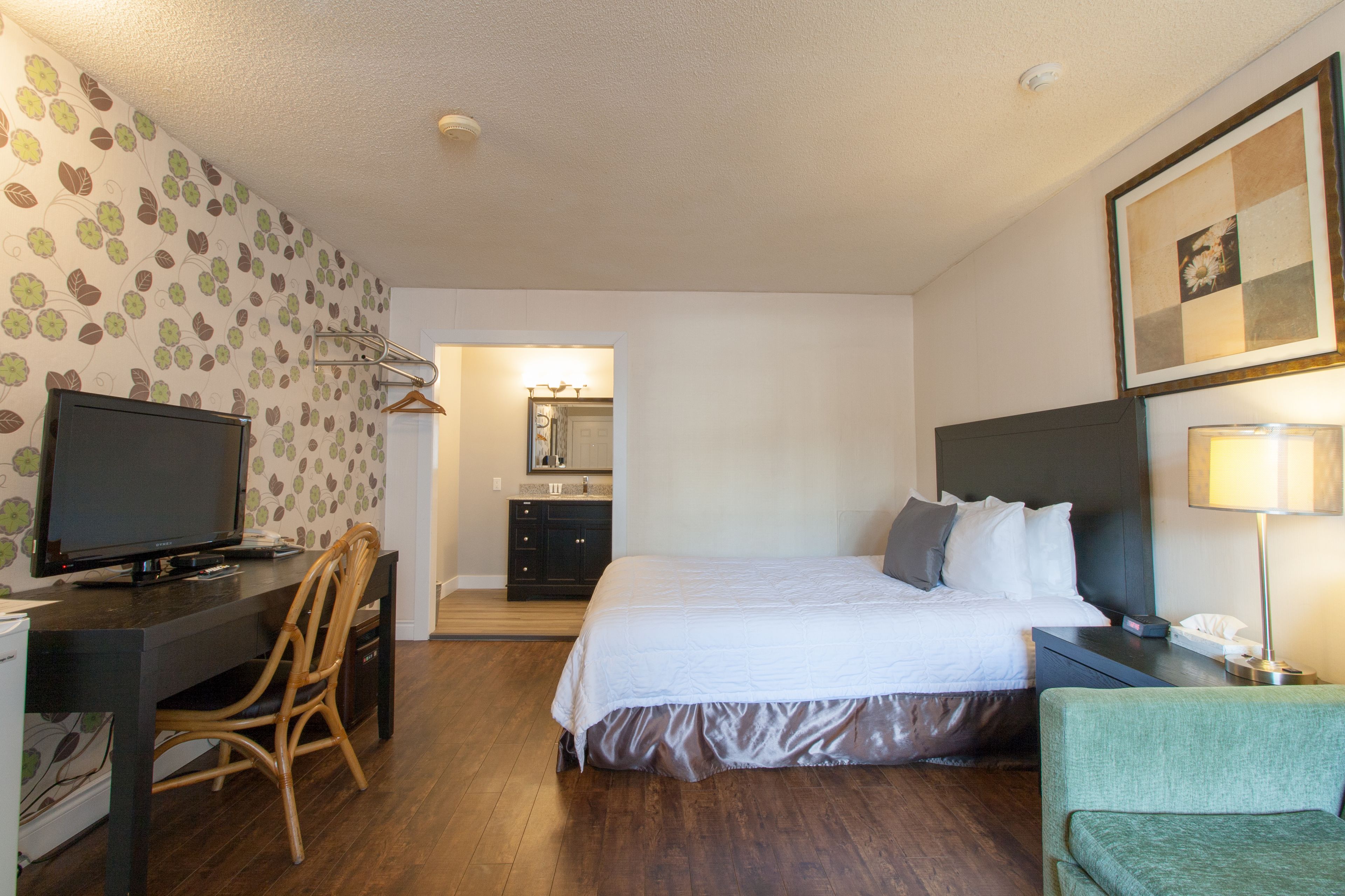 Een hotelkamer met een bed, een bureau met een televisie, een stoel, een nachtkastje met een lamp, en een badkamer die door een open deur zichtbaar is.