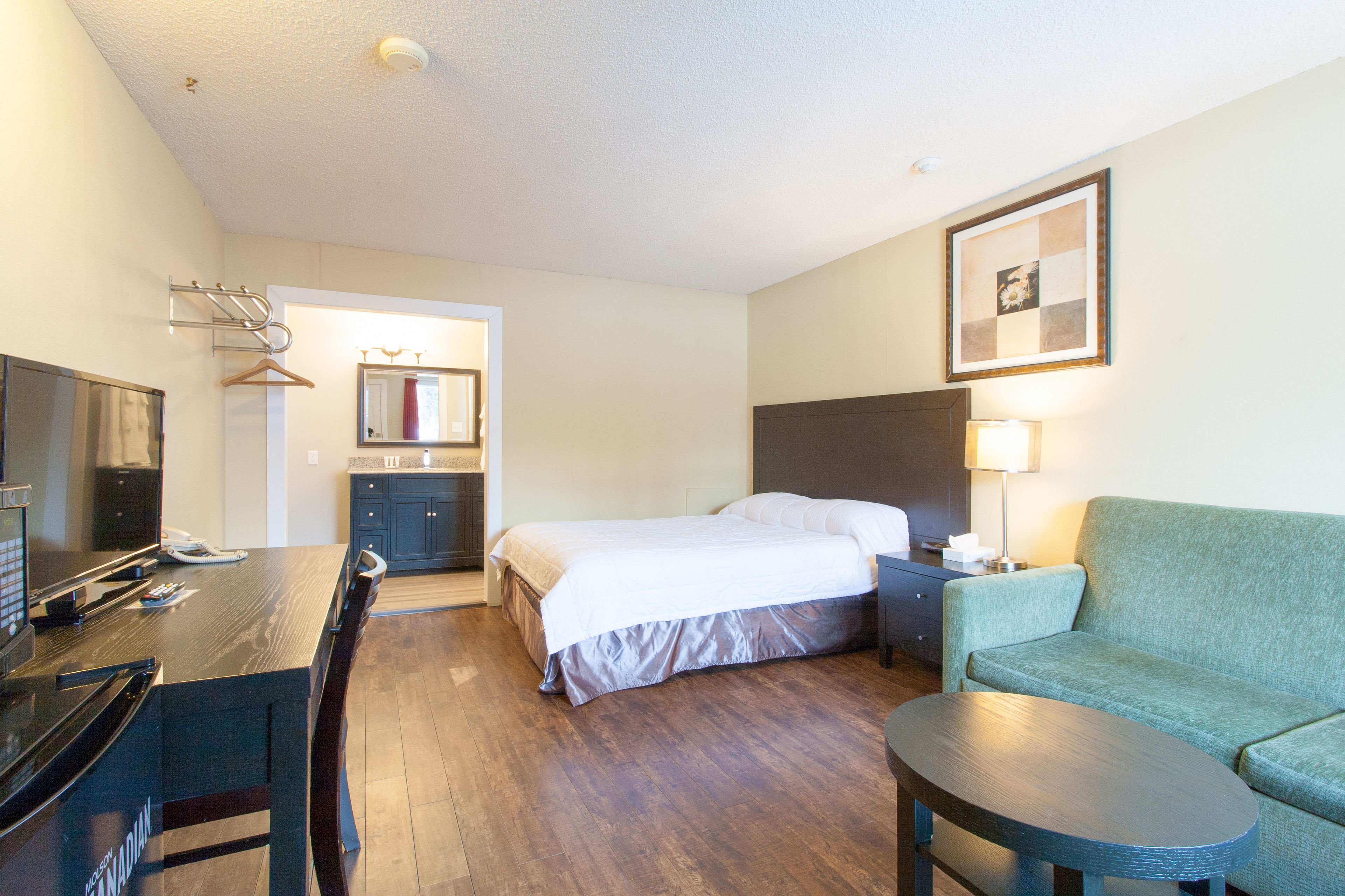 A hotel room with a bed, a desk with a computer, a TV, a sofa, and a lamp.