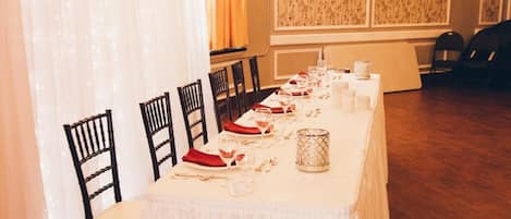 A long dining table set for a meal with chairs, a chandelier, and patterned wallpaper.
