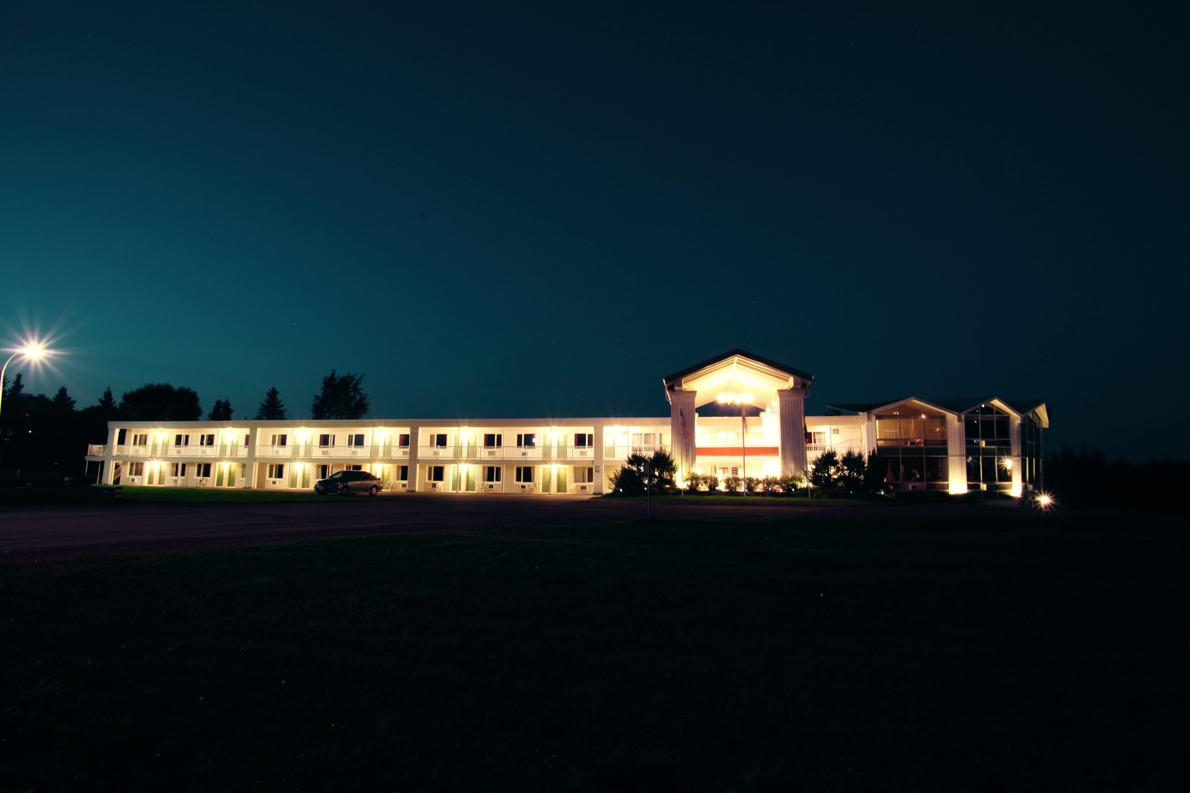 Een motel met meerdere kamers, een centraal gebouw met een opvallend dak en een parkeerplaats.
