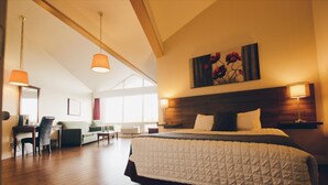 Une chambre spacieuse dotée d’un grand lit, d’un bureau et d’une chaise, avec un plancher en bois et un plafond haut.