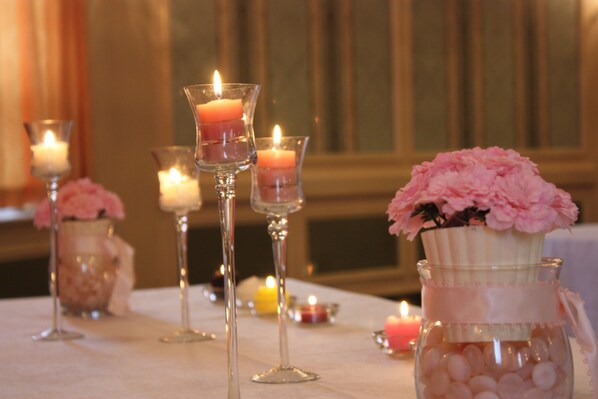 Une table ornée de bougies dans des photophores en verre et d’un vase rempli de fleurs roses.