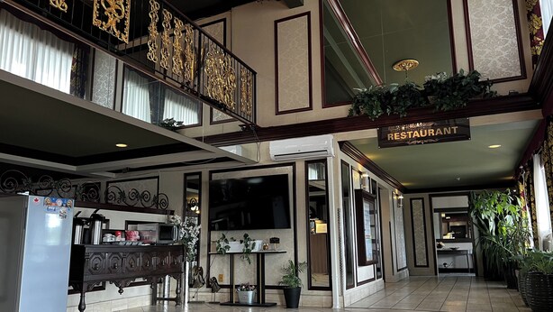 Un hall d’hôtel avec un panneau indiquant la présence d’un restaurant, un lustre et un escalier orné de balustrades décoratives.