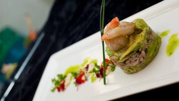 A plate with a seafood dish, possibly a sushi roll, garnished with a green sauce and a green vegetable.