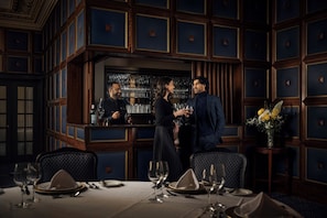 A bar area with a dark wood panel design, a bar counter, and a seating area with tables set for dining. - The Union Club of British Columbia (Victoria)