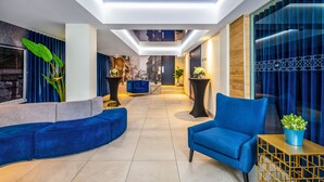 Un hall d’entrée moderne avec un canapé bleu, un fauteuil bleu et une petite table agrémentée d’une plante.