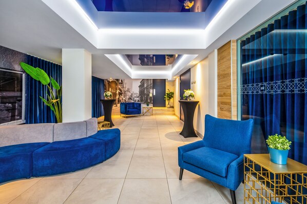 Un moderno hall de entrada con un sofá azul, un sillón azul y una pequeña mesa con una planta.