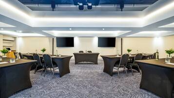 Una sala de conferencias moderna con un estampado geométrico en la alfombra, varias mesas, sillas y dos grandes televisores de pantalla plana montados en las paredes.