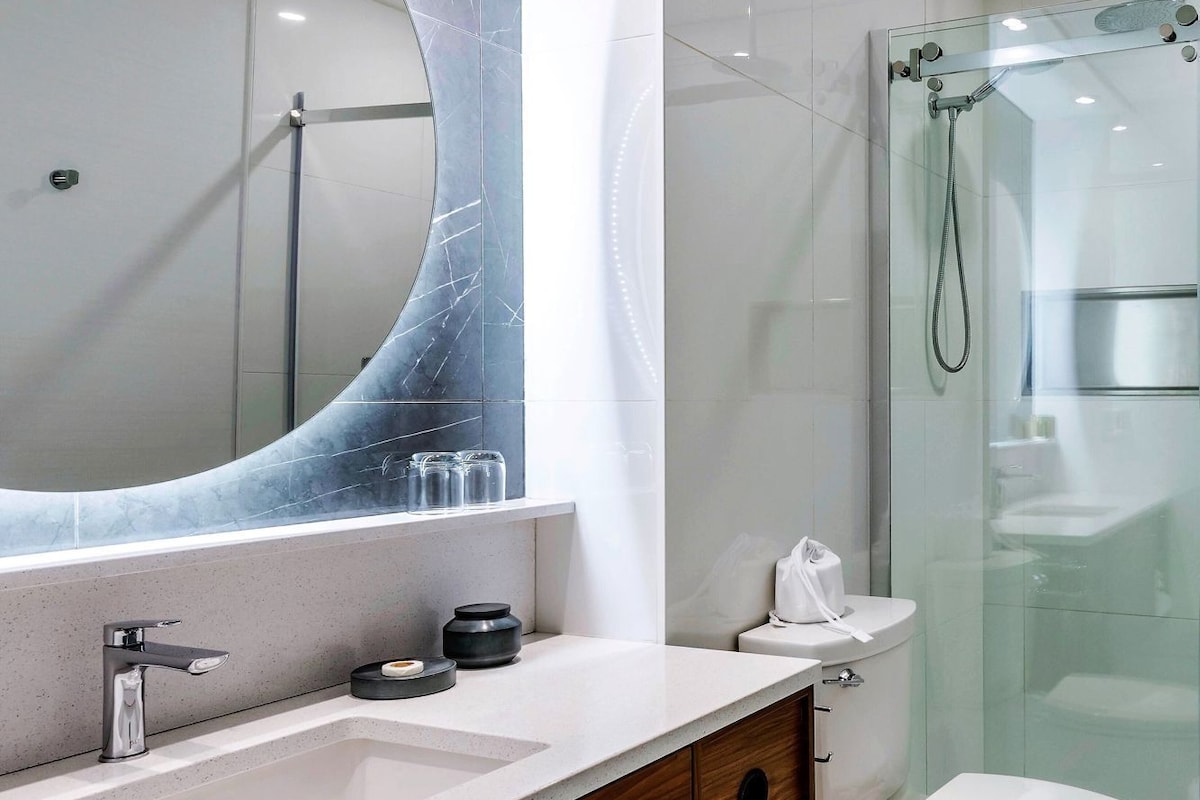 A modern bathroom with a large mirror, a sink, a toilet, and a shower area.