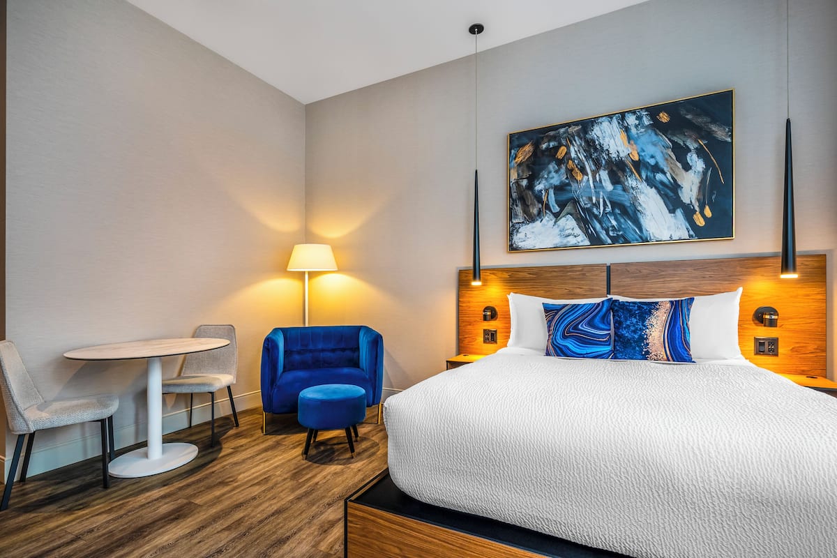 A hotel room with a bed, a small round table, two chairs, a blue sofa, and a painting on the wall.