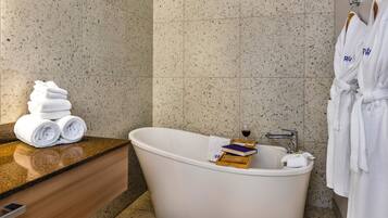 Ein modernes Badezimmer mit einer freistehenden Badewanne, einem Stapel gefalteter Handtücher und zwei weißen Bademänteln, die auf einem Gestell hängen.