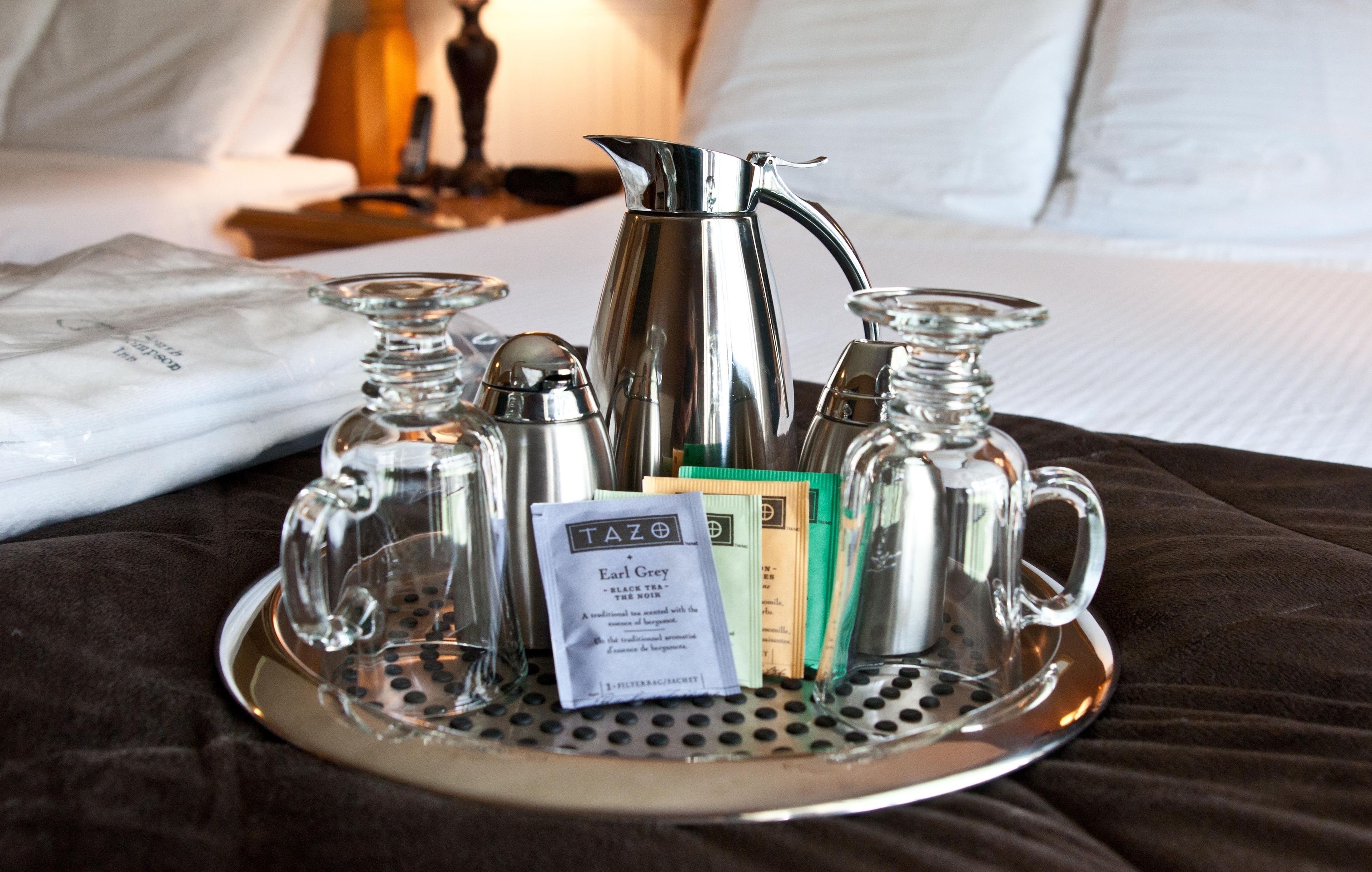 A tray with a silver pitcher, two small bottles, and a packet of Earl Grey tea on a bed.
