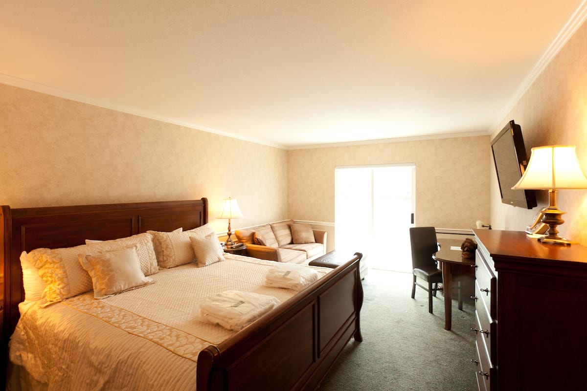 A hotel room with a large bed, a desk, a chair, a television, and a lamp.