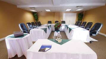 Un salón de conferencias con una larga mesa, varias sillas, un proyector y un arreglo floral.