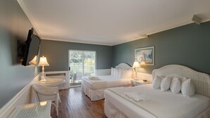 A hotel room with two beds, a sitting area with a chair, a table, and a window with a view of greenery. - South Thompson Inn & Conference Centre (Kamloops)