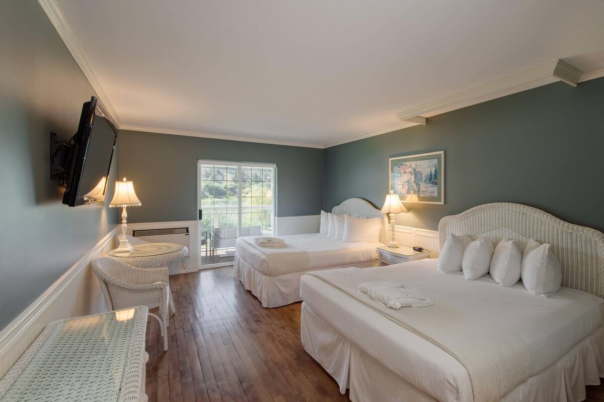 A hotel room with two beds, a sitting area with a chair, a table, and a window with a view of greenery.