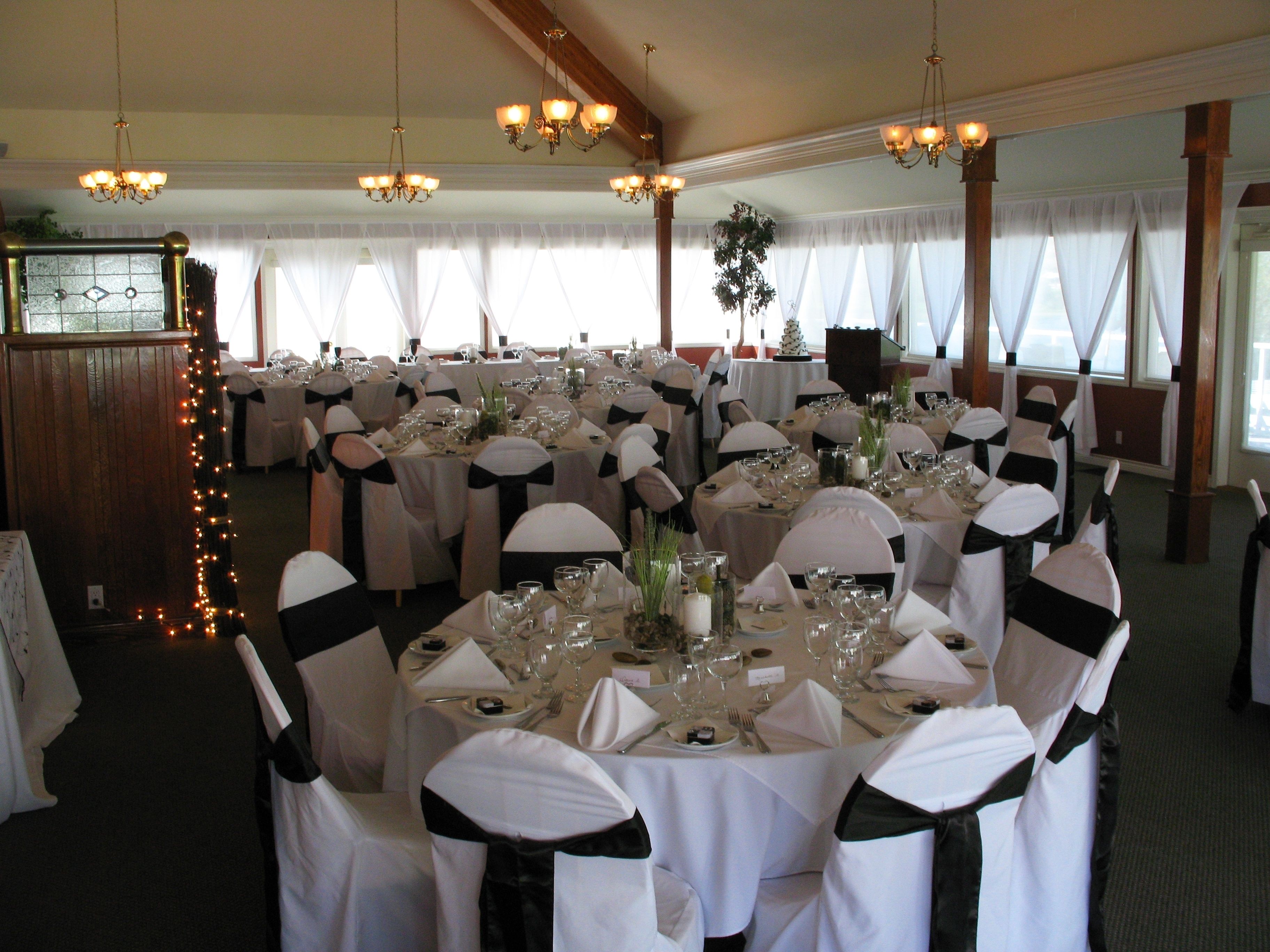 Een feestzaal met ronde tafels gedekt voor een formeel evenement, met kroonluchters, witte tafellakens en zwarte linten op de stoelen.