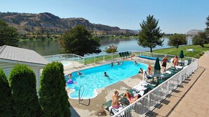 A swimming pool with people, surrounded by trees and a view of hills. - South Thompson Inn & Conference Centre (Kamloops)