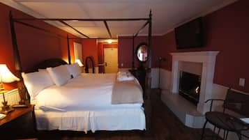 A four-poster bed with white linens, a fireplace, and a mirror above it.