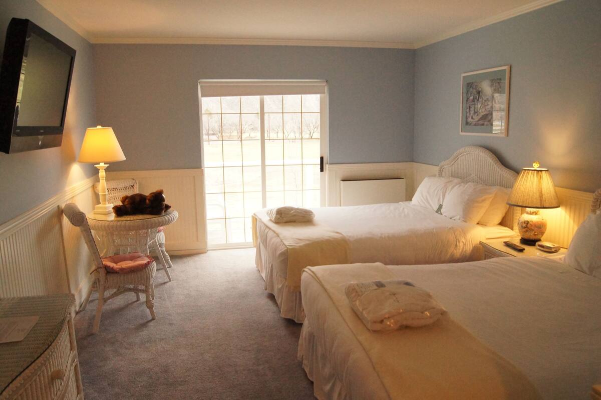 A hotel room with two beds, a chair, a table, and a window.