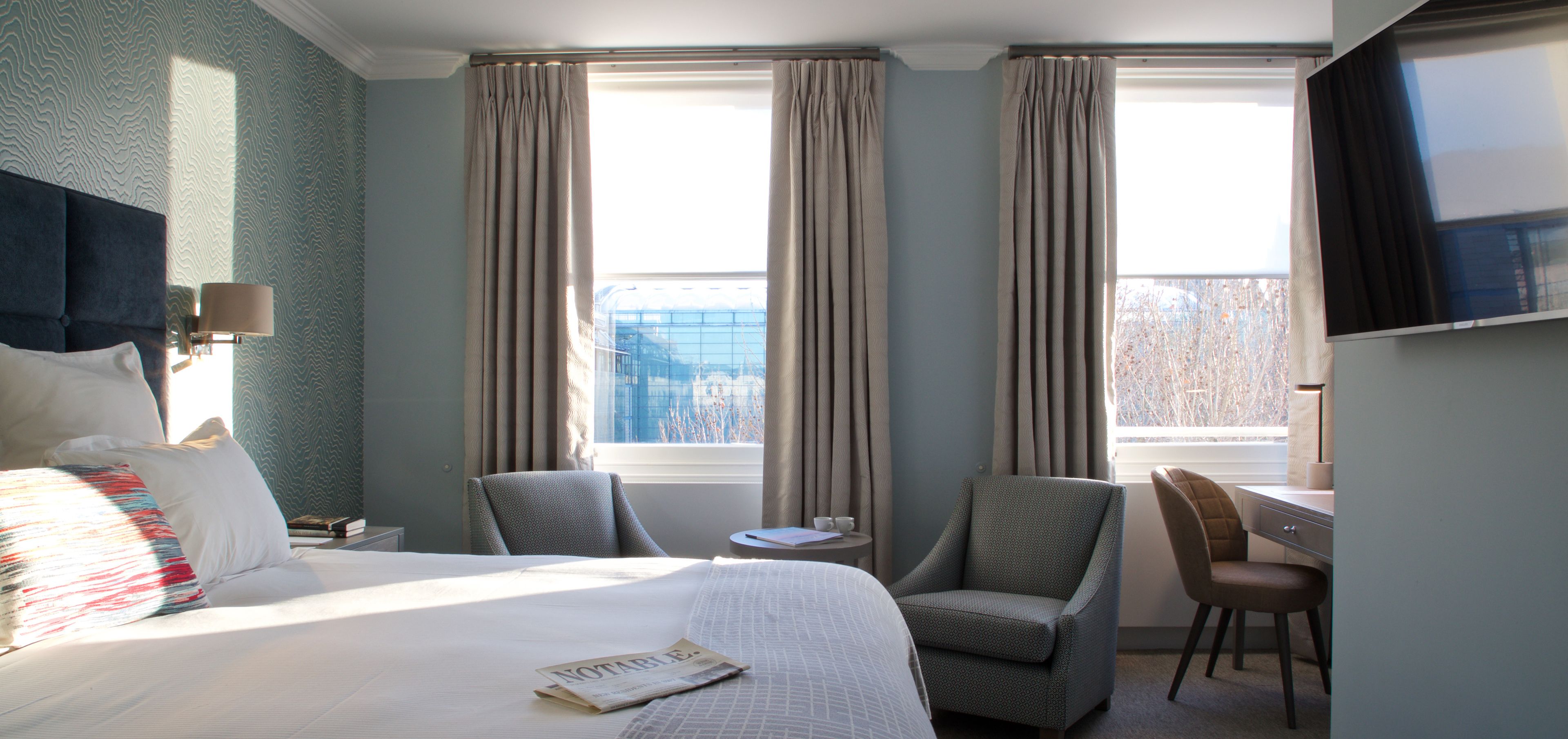 Una habitación de hotel con una cama, dos sillas, un escritorio y un televisor.