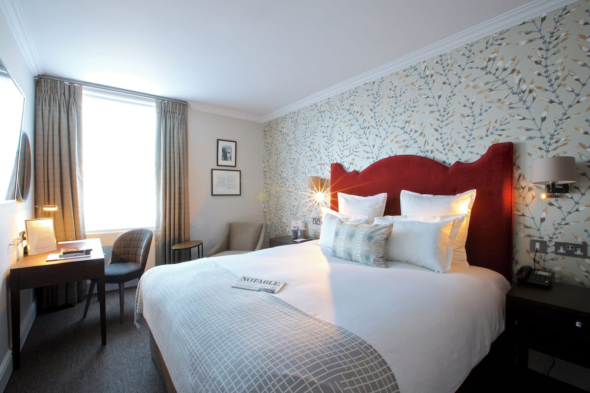 Habitación de hotel con una cama grande, un escritorio con silla, una mesita y una lámpara.