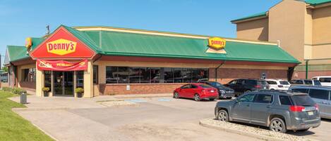 Un restaurante Denny's con techo verde y un estacionamiento con varios autos.