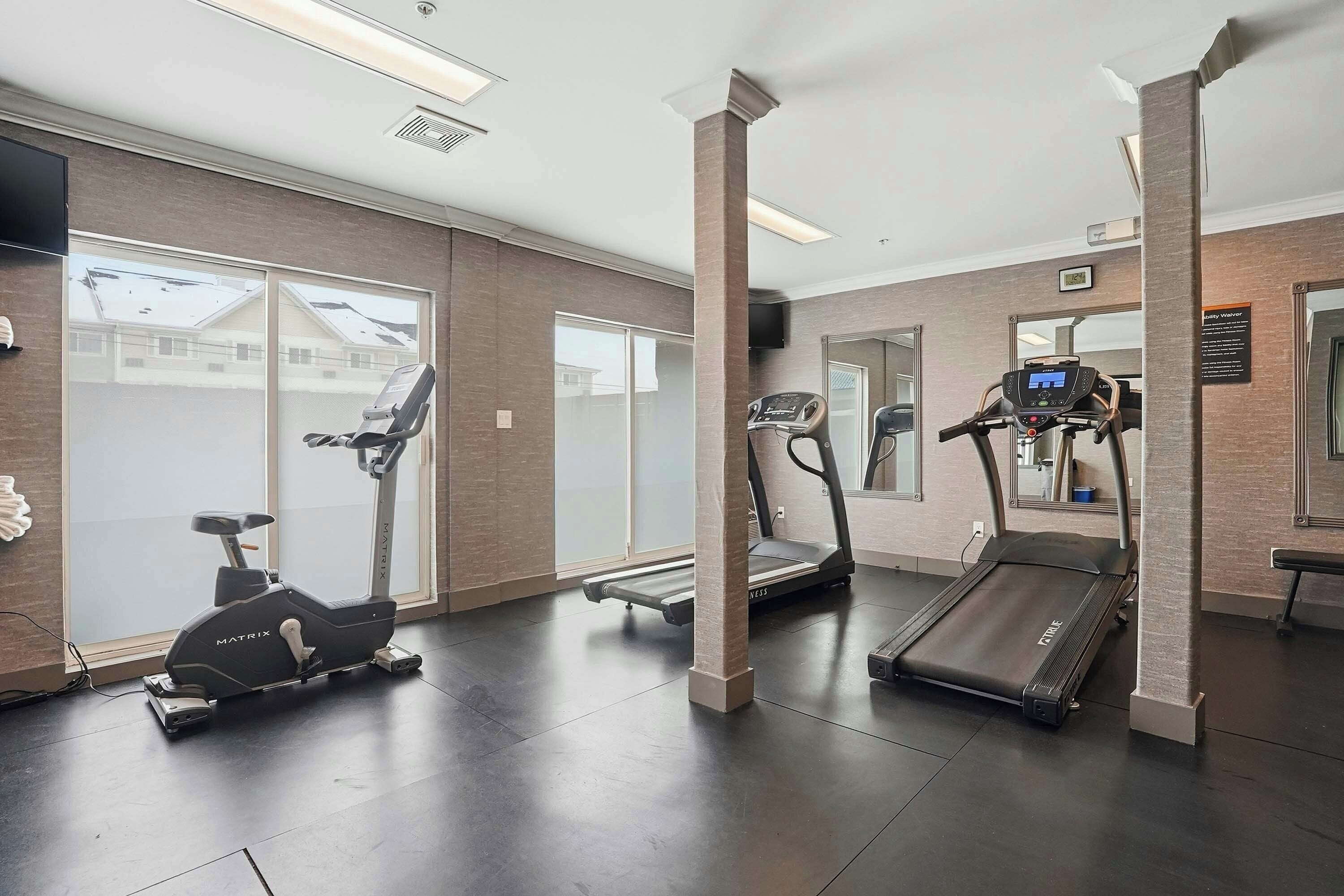 Een fitnessruimte met trainingsapparatuur, waaronder een loopband, een elliptische trainer en een hometrainer.