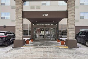Entrada de un edificio con un cartel con el número 310, puertas de cristal y un estacionamiento con dos coches.
