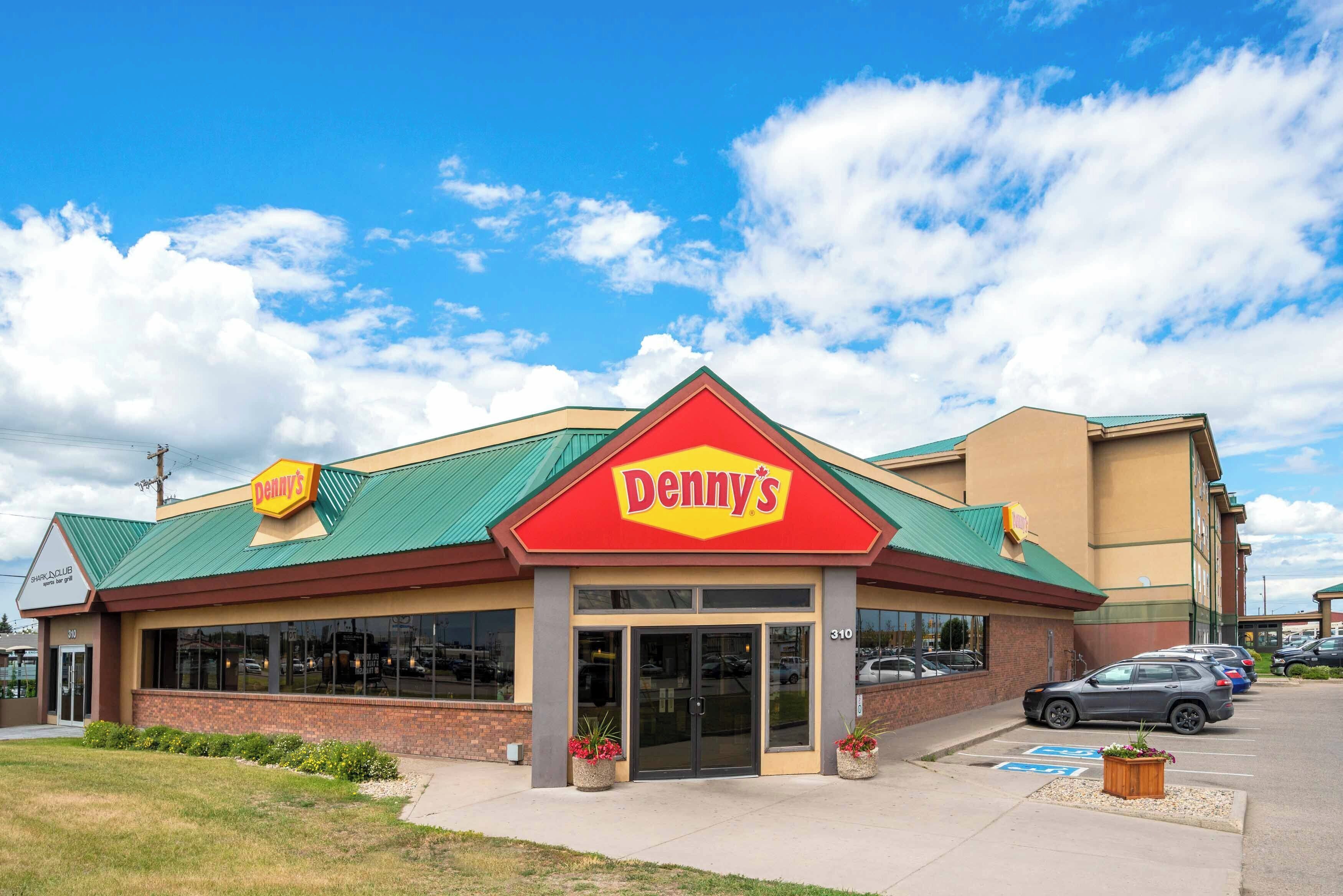 Un restaurant Denny's doté d’un toit végétalisé, d’une enseigne rouge et jaune et d’un parking rempli de voitures.