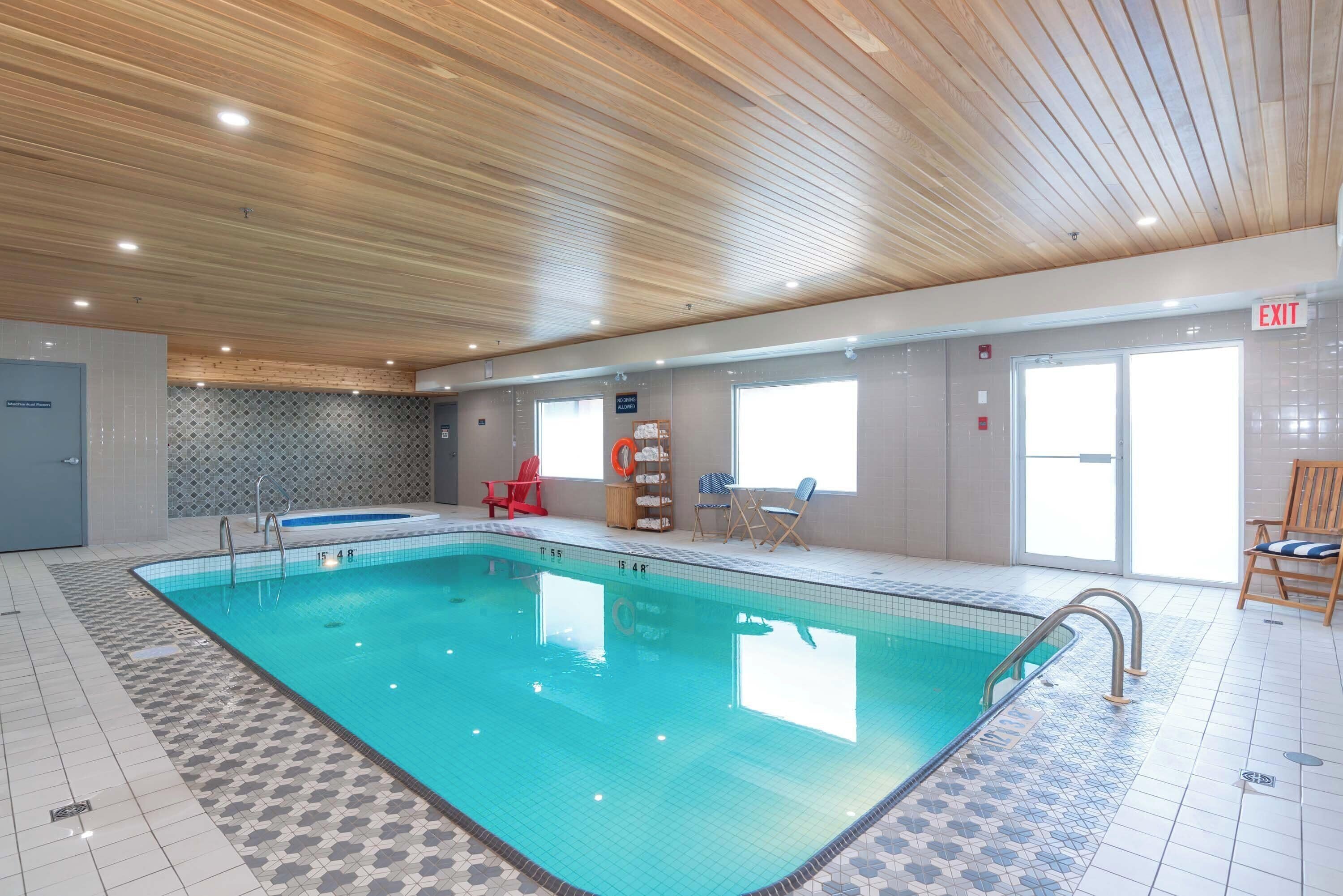 Ein beheiztes Hallenbad mit Fliesenboden, Holzbalkendecke und einem gut sichtbaren Ausgangsschild.