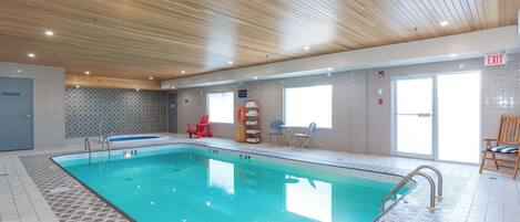 An indoor swimming pool with tiled flooring, wooden ceiling, and a clear exit sign.