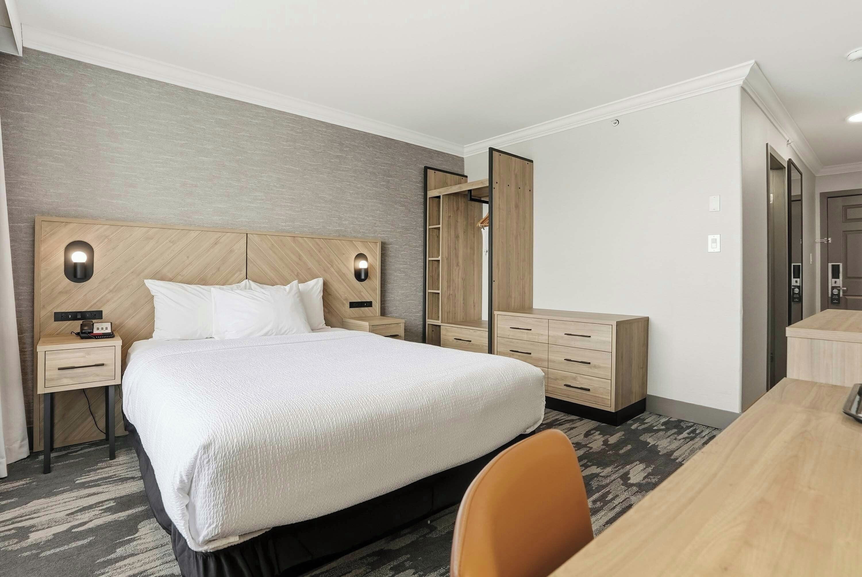 A hotel room with a large bed, bedside tables, a desk, and a wardrobe.