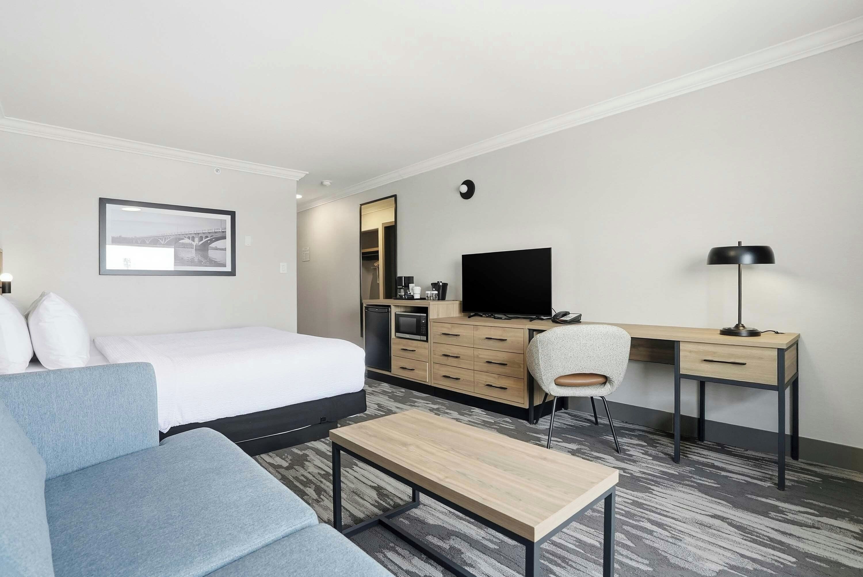 Une chambre d’hôtel avec un lit, un bureau, une chaise, une télévision et une petite table.