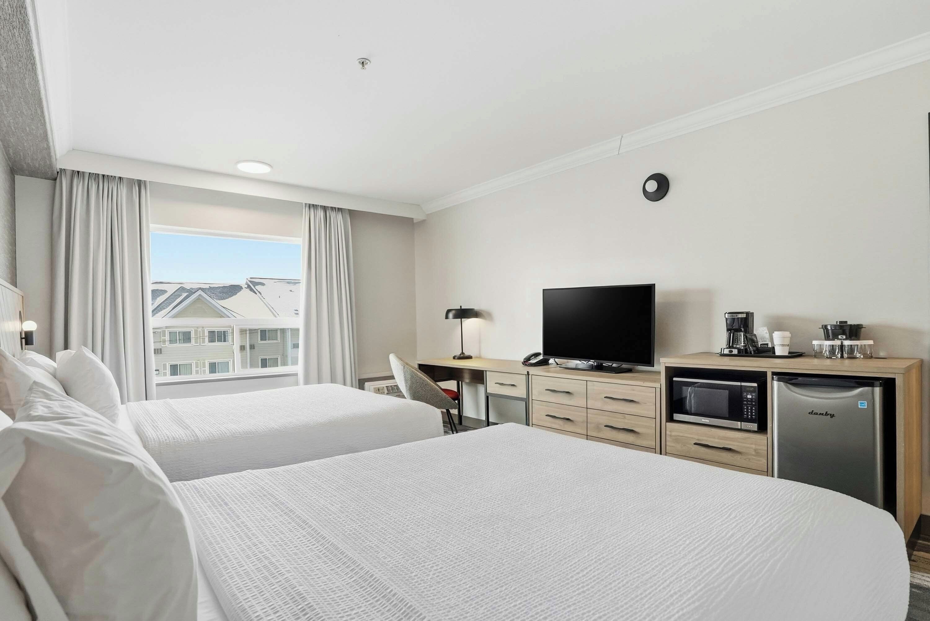A hotel room with two beds, a desk with a TV, a microwave, and a refrigerator.