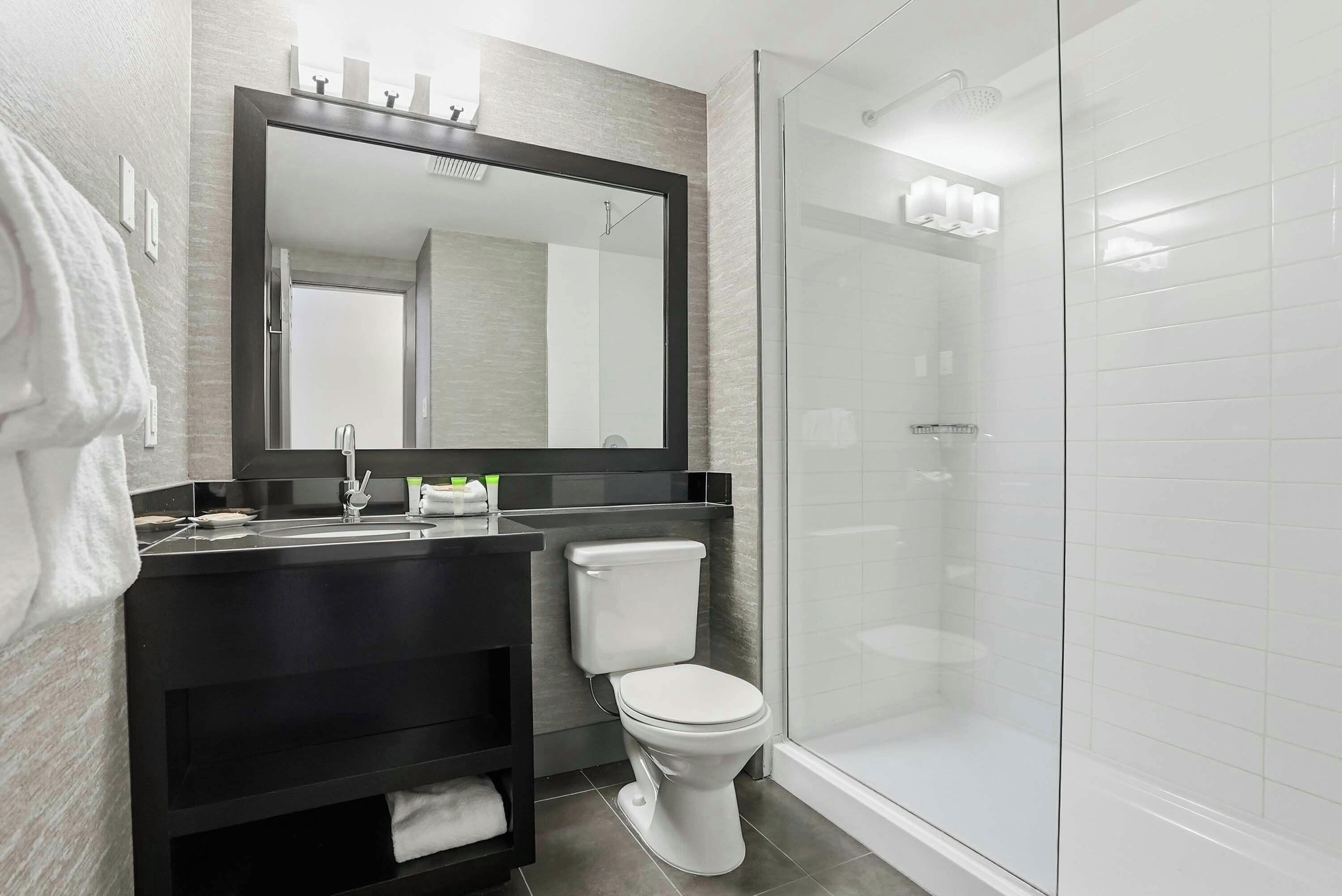 Un baño moderno con ducha envuelta en vidrio, inodoro blanco y tocador negro con espejo.