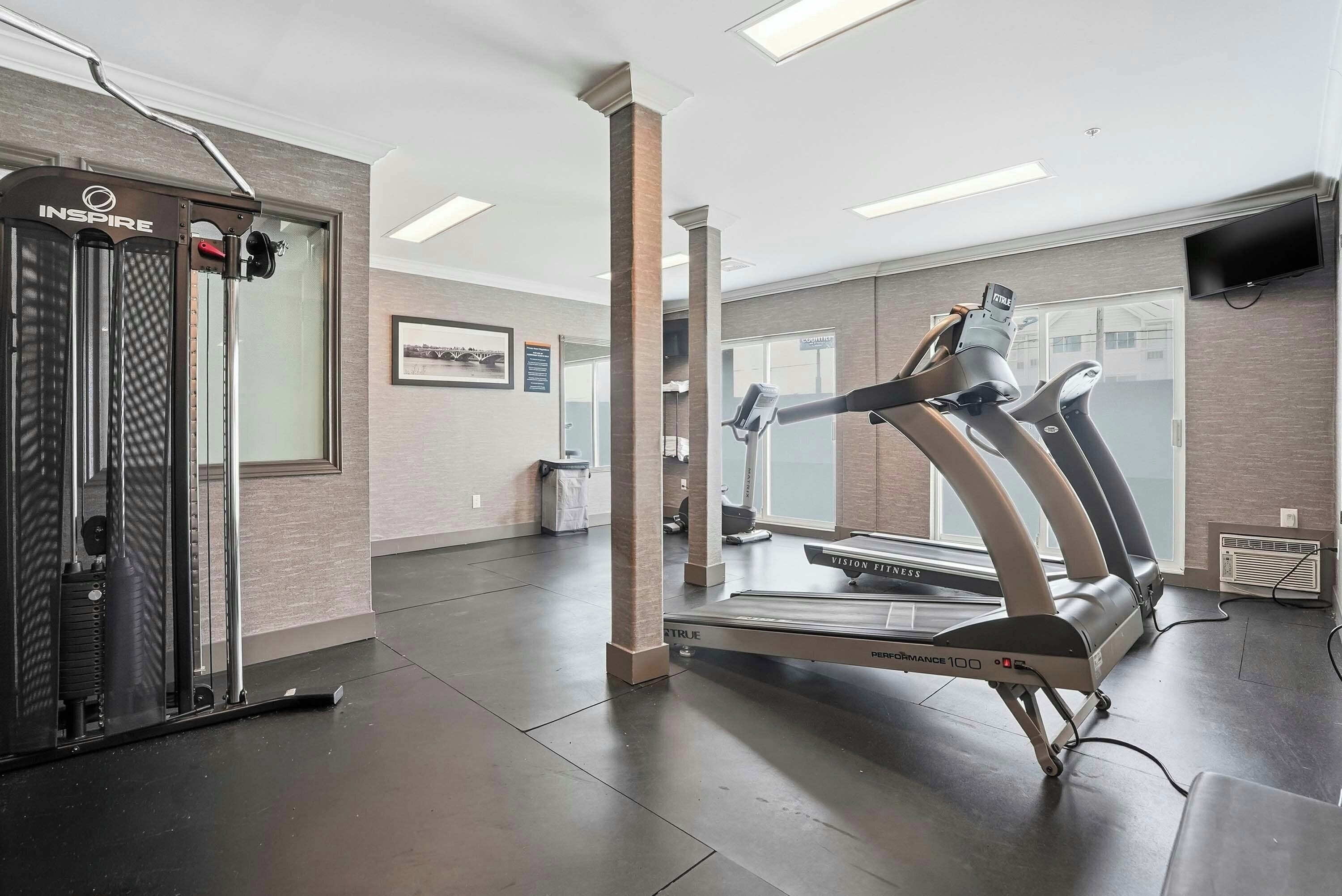 A gym with a treadmill, a weight machine, and a wall-mounted TV.
