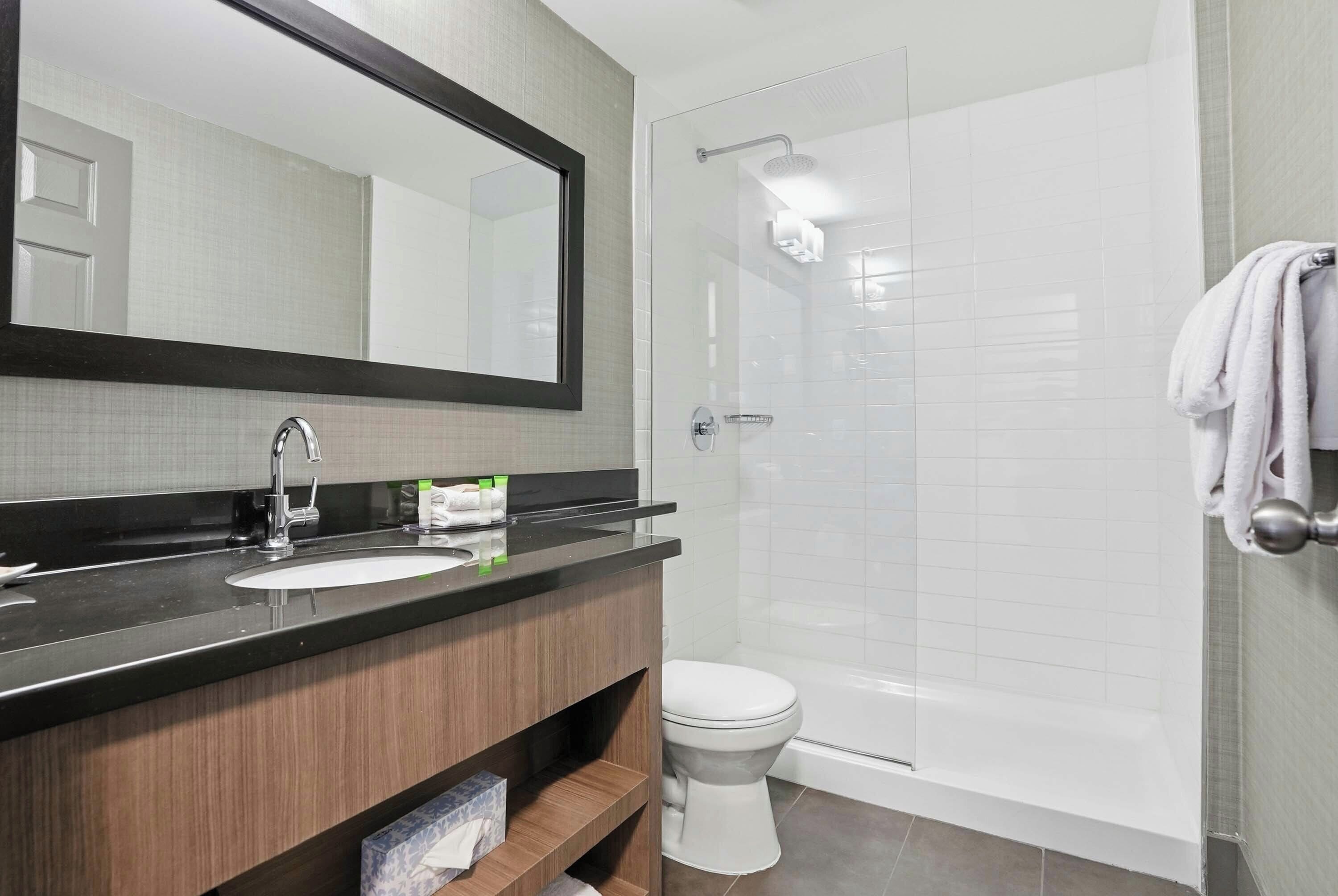 Un baño moderno con un espejo grande, un lavabo, un inodoro y una ducha.