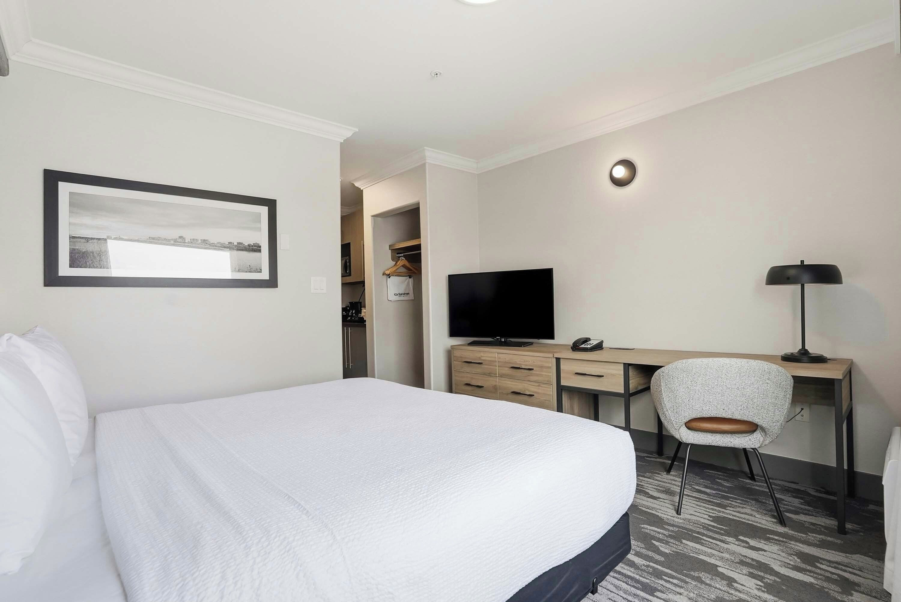 A hotel room with a large bed, a desk with a chair, a television, and a framed picture on the wall.