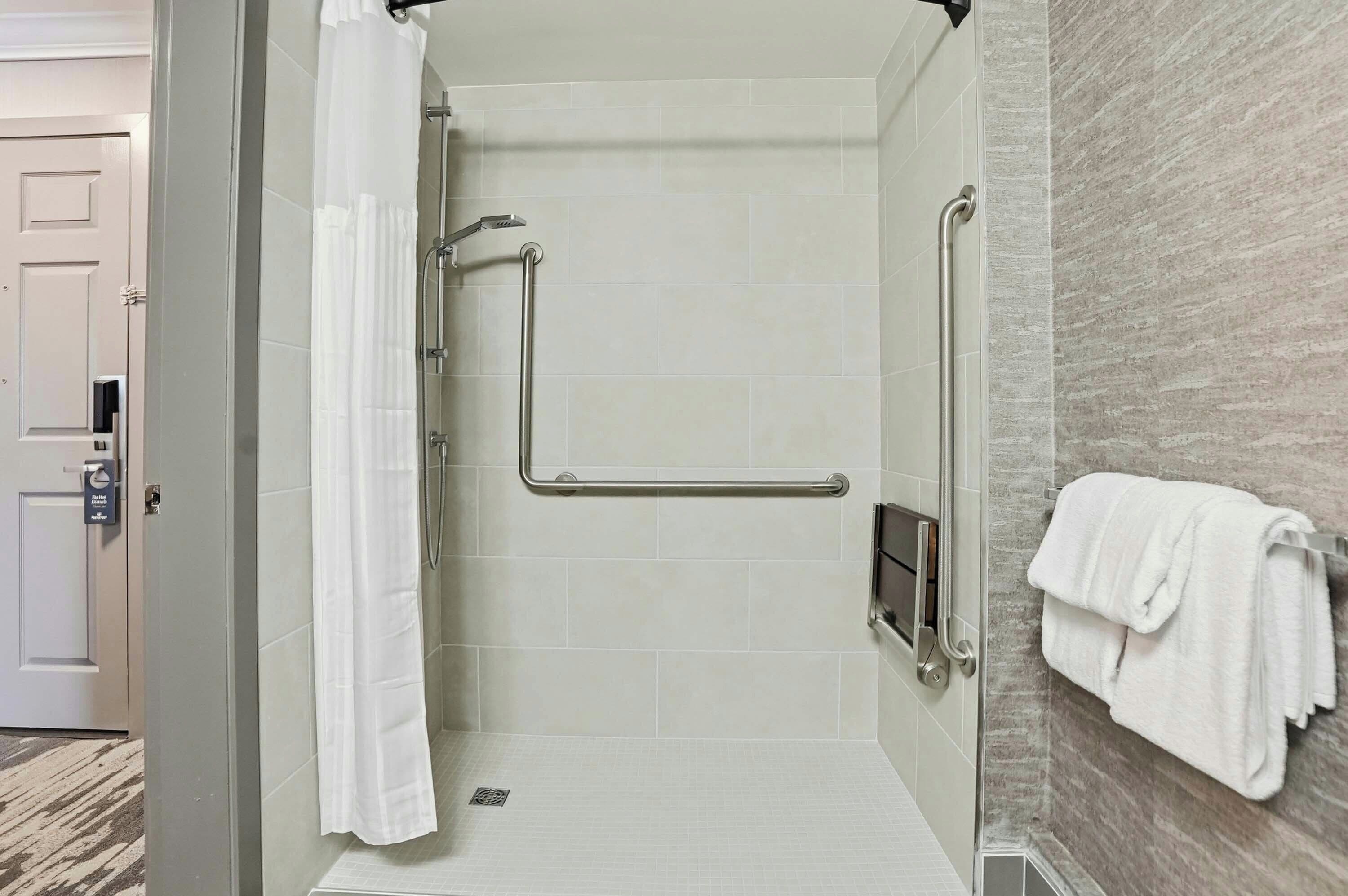 A modern bathroom with a walk-in shower, grab bars, and a towel rack.