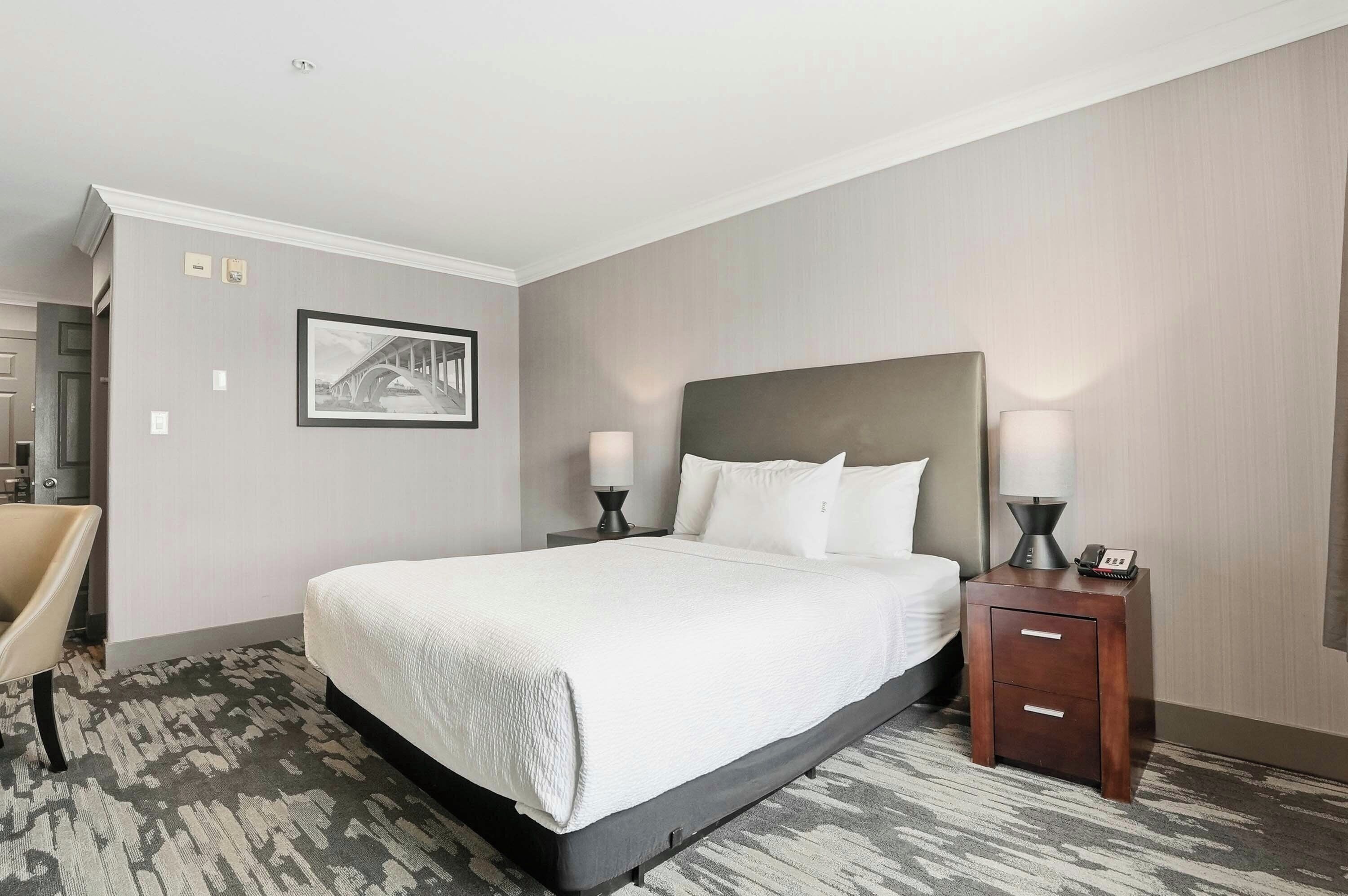 A hotel room with a large bed, two bedside tables with lamps, a chair, and a framed picture on the wall.