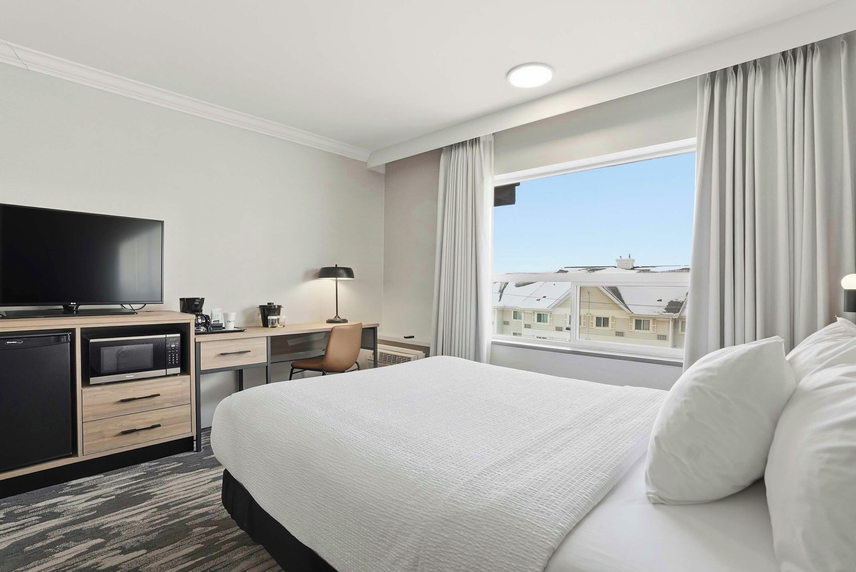 Habitación de hotel con cama, escritorio con computadora, televisor y ventana con cortinas.