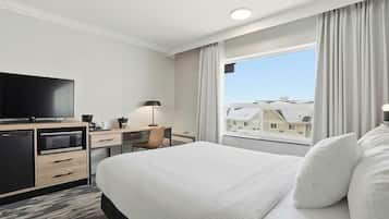 Habitación de hotel con cama, escritorio con computadora, televisor y ventana con cortinas.