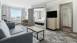 Une chambre d’hôtel avec un canapé, une petite table, une télévision, un lit, un bureau et une salle de bain équipée d’un rideau de douche.