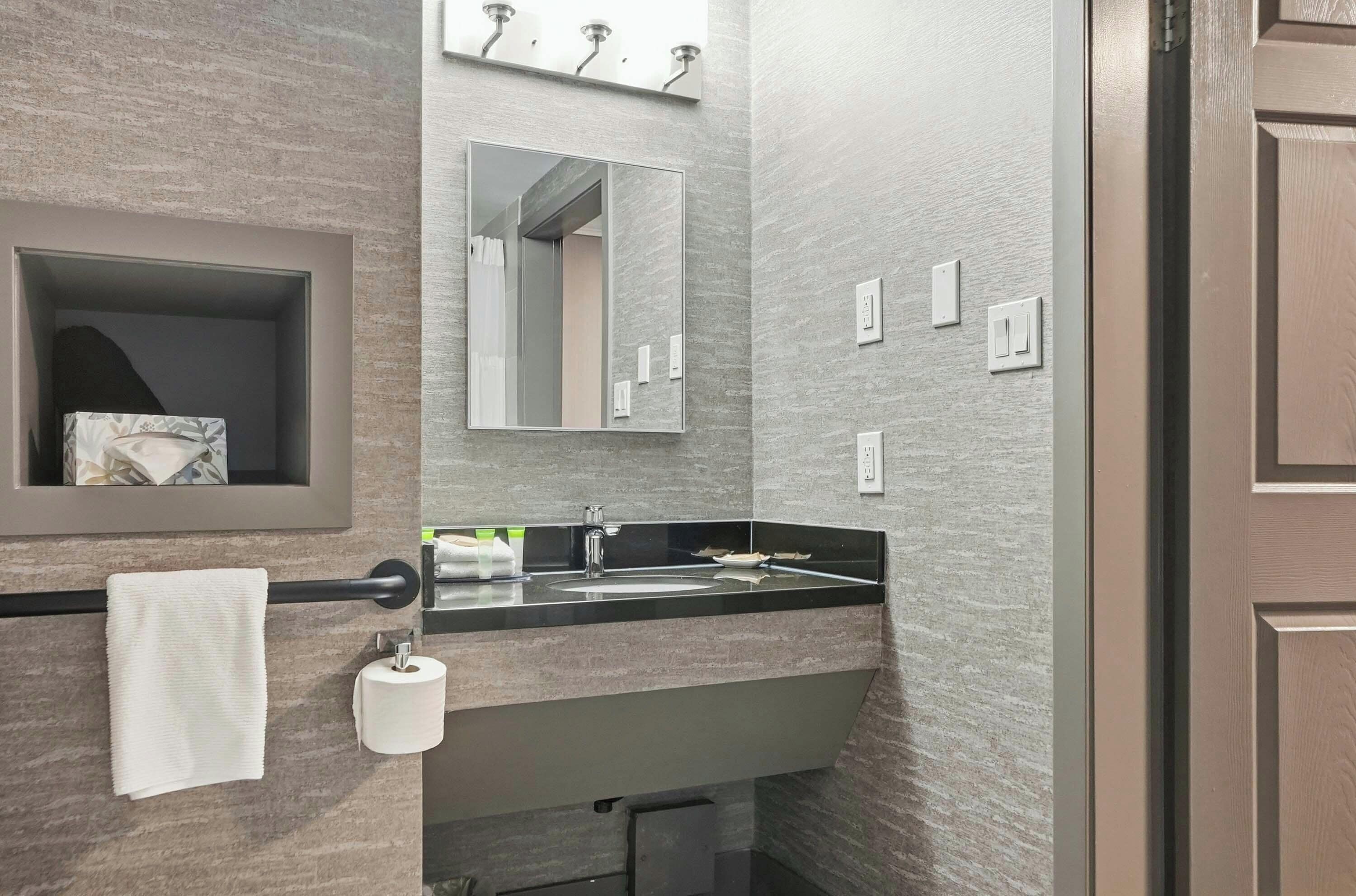 A modern bathroom with a marble wall, a sink, a mirror, and a towel rack.